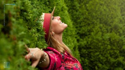 Kvinde med stråhat, der lænder sig op ad en grøn hæk.